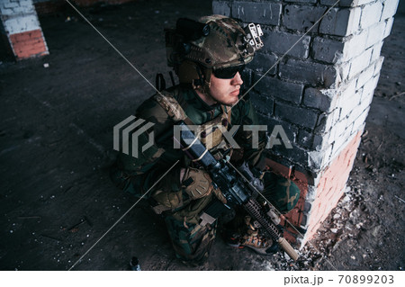 Military soldier in the form holds in the hands an assault rifle, check possible enemies around the corner 70899203