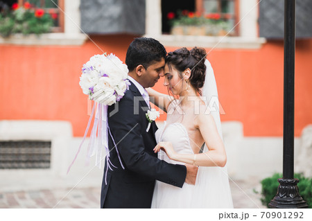 Gorgeous happy couple standing close to each other and looking in eyes at old city background, wedding photo, European city, wedding day in Lviv 70901292