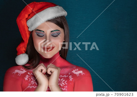 A young brunette woman with ideal art make-up and in a Santa Claus hat makes a wish with closed eyes A young brunette woman with ideal art make-up and in a Santa Claus hat makes a wish with closed eyes 70901623