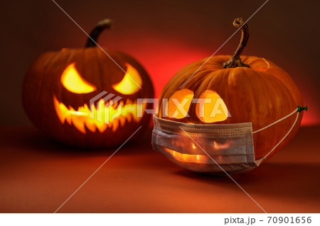 Halloween concept with angry pumpkin lamp and surgical or protection mask. Covid-19 and Halloween Halloween concept with angry pumpkin lamp and surgical or protection mask. Covid-19 and Halloween 70901656