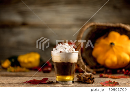 Pumpkin spice latte with cinamon powder and delicious flavours on the old textured wood table with colorful dry leaves and pumpkins 70901709