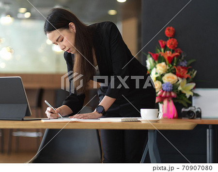 Businesswoman working on paperwork while standing at workplace 70907080