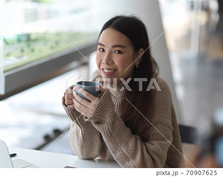Female student holding coffee cup while relaxed sitting in cafe Female student holding coffee cup while relaxed sitting in cafe 70907625