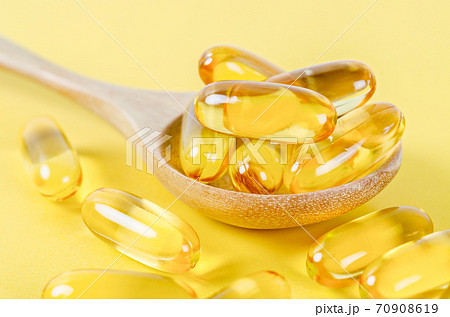 Fish oil capsules in wooden spoon. 70908619