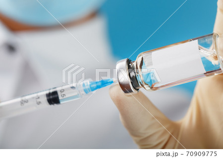 A doctor in rubber gloves holds an ampoule with a vaccine and a syringe, close-up. A doctor in rubber gloves holds an ampoule with a vaccine and a syringe, close-up. 70909775