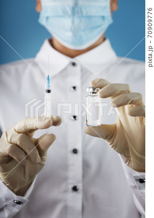 A doctor in rubber gloves holds an ampoule with a vaccine and a syringe, close-up. 70909776
