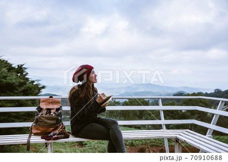 The girl is sitting relaxing at the natural mountain viewpoint and writing a record of her winter travel. smiled happy writing a diary. The girl is sitting relaxing at the natural mountain viewpoint and writing a record of her winter travel. smiled happy writing a diary. 70910688
