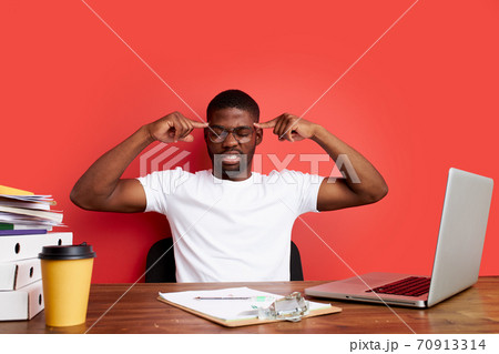 overworked unhappy and frustrated young african man in stress sitting at office desk 70913314