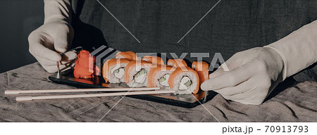 Hands in rubber gloves serve sushi on a black stand. Sushi menu. Hands in rubber gloves serve sushi on a black stand. Sushi menu. 70913793