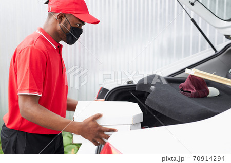 side view on young courier in mask putting order in boxes at car 70914294