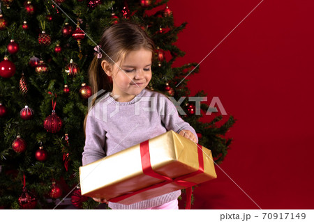 Smiling little toddler girl holding gift box on background of Christmas tree 70917149