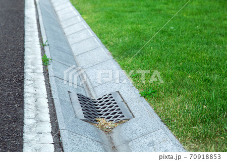 gutter of a stormwater drainage system in perspective on the side of an road with markings and lawn. 70918853