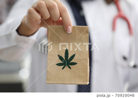 Doctor with strethoscope around neck holds paper bag with marijuana closeup Doctor with strethoscope around neck holds paper bag with marijuana closeup 70920046