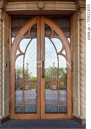 The front door on the facade of the building is wooden brown frame with glass inserts with a pattern, the double door in retro style. The front door on the facade of the building is wooden brown frame with glass inserts with a pattern, the double door in retro style. 70921820