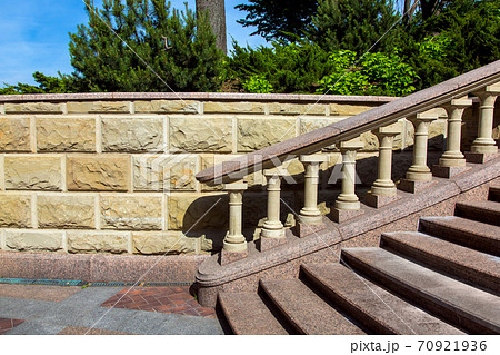 Baroque staircase with marble steps and stone balustrades under the railing on the background of a wall of stone tiles and plants in the background. Baroque staircase with marble steps and stone balustrades under the railing on the background of a wall of stone tiles and plants in the background. 70921936