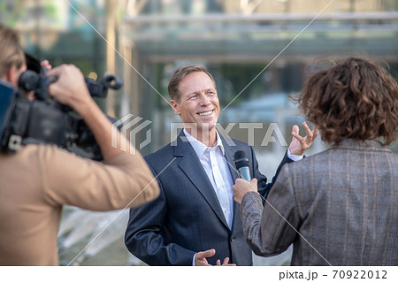 Rear view of operator filming curly female journalist interviewing smiling businessman 70922012