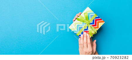 Woman arms holding gift box with colored ribbon on blue table background, top view and copy space for you design 70923282