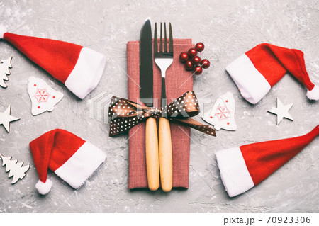 Festive set of fork and knife on cement background. Top view of new year decorations and santa clothes and hat. Close up of Christmas concept Festive set of fork and knife on cement background. Top view of new year decorations and santa clothes and hat. Close up of Christmas concept 70923306