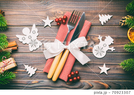 Top view of utensils on festive napkin on wooden background. Christmas decorations with dried fruits and cinnamon. Close up of New year dinner concept Top view of utensils on festive napkin on wooden background. Christmas decorations with dried fruits and cinnamon. Close up of New year dinner concept 70923307