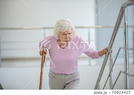 Elderly woman with a walking stick slowly going upstairs Elderly woman with a walking stick slowly going upstairs 70923427