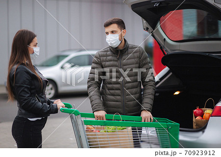 Husband and his wife in protective mask after buying food in grocery store or supermarket during quarantine. Side view. Food shopping during coronavirus Covid-19 quarantine Husband and his wife in protective mask after buying food in grocery store or supermarket during quarantine. Side view. Food shopping during coronavirus Covid-19 quarantine 70923912