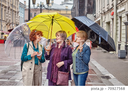 Senior women with umbrellas talk on street. Senior women with umbrellas talk on street. 70927568
