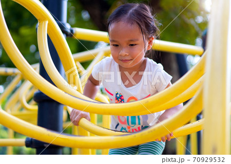 Asian girl is climbing on a playground equipment in a school. 70929532