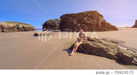 Young woman in bikini sitting on a rock on a beach full of cliffs 70929573