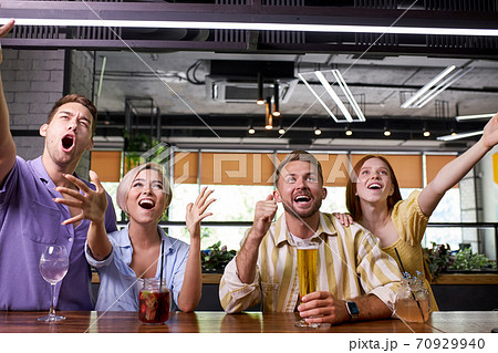happy friends drinking beer, watching sport game or football match together in bar 70929940