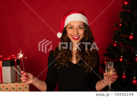 Smiling woman in santa hat with xmas gifts tree on red background, copy space Smiling woman in santa hat with xmas gifts tree on red background, copy space 70930249
