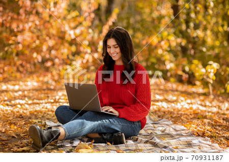 Positive young woman working on laptop computer, browsing internet at park in autumn 70931187