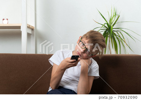 Bored boy with glasses switches TV channels. Child is watching TV. Bored boy with glasses switches TV channels. Child is watching TV. 70932090