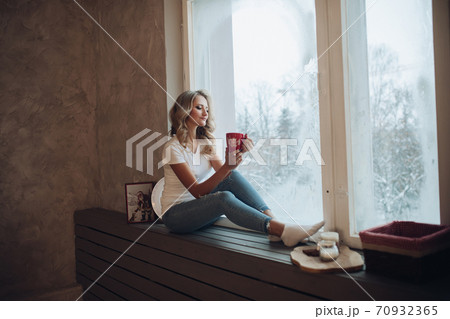 Beautiful blonde sitting on window sill with mug. 70932365