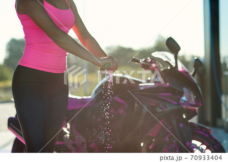 Close up woman's hands squeeze moisture out of the rag while wipes sport motorcycle at self service car wash. 70933404
