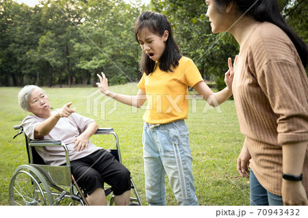Unhappy asian teen granddaughter dissuade her family from a fight something money,angry senior mother and daughter arguing violently,shouting quarreling at park, borrowing money and not returning it 70943432