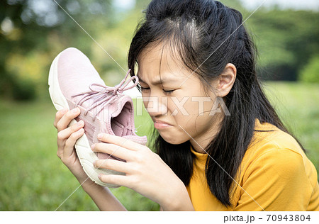Unhappy asian female teenage is sniffing her sneakers,hold stinky shoe in her hand with disgust,unpleasant smell because of hot weather or after exercise,sad child girl with bad smell,accumulated dirt 70943804