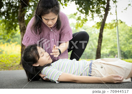 Sick daughter is fainted and fallen on floor,asian mother help,take care,child girl with heat stroke,high temperature,female unconscious fell to the ground suffer from sunburn very hot in outdoor park 70944517