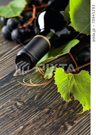 Unopened red wine bottle, vine twig, and ripe grapes on an old wooden table. Unopened red wine bottle, vine twig, and ripe grapes on an old wooden table. 70945293