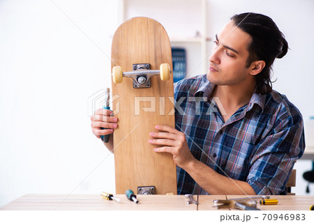 Young man repairing skateboard at workshop 70946983