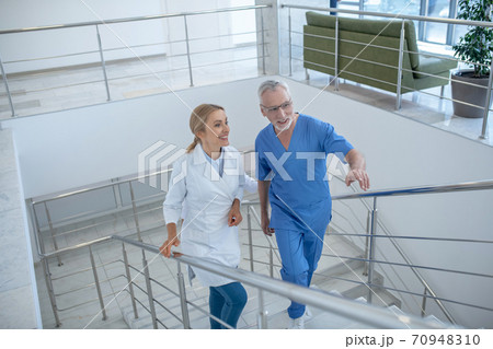 Male and female doctors walking upstairs, having friendly conversation Male and female doctors walking upstairs, having friendly conversation 70948310