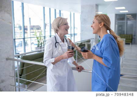 Two smiling female medical workers leaning on stair railing, drinking coffee 70948348