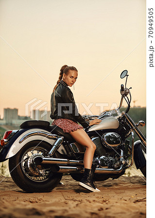 Biker girl in a leather jacket on a motorcycle looking at the sunset. Biker girl in a leather jacket on a motorcycle looking at the sunset. 70949505