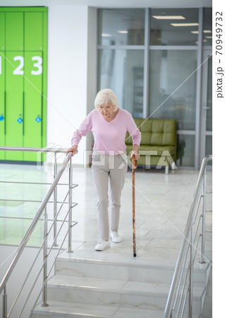 Grey-haired woman with a walking stick going downstairs 70949732