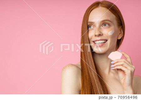 Portrait of young woman applying face cream and cleansing face with sponge Portrait of young woman applying face cream and cleansing face with sponge 70956496