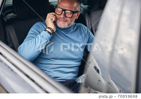Car passenger with his cellphone looking away 70959698