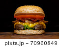 Close up fresh tasty the hamburger with cheese, tomato, beef, bacon and green salad vegetable, selective focusing technical, wooden table and darkness background. 70960849