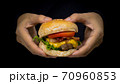 Hands holding the fresh tasty hamburger with cheese, tomato, beef, bacon and green salad vegetable, selective focusing technical on isolated black shadow background 70960853