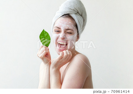 Minimal beauty portrait woman girl in towel on head applying white nourishing mask or creme on face, green leaf in hand isolated white background. Skincare cleansing eco organic cosmetic spa concept. 70961414