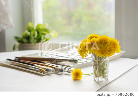 A bouquet of dandelions is on the table with paints and brushes for painting. The concept of art. Summer still life A bouquet of dandelions is on the table with paints and brushes for painting. The concept of art. Summer still life 70962686