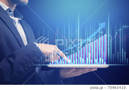 Man in suit holds tablet with futuristic hologram graphic and works at growth chart Man in suit holds tablet with futuristic hologram graphic and works at growth chart 70963410
